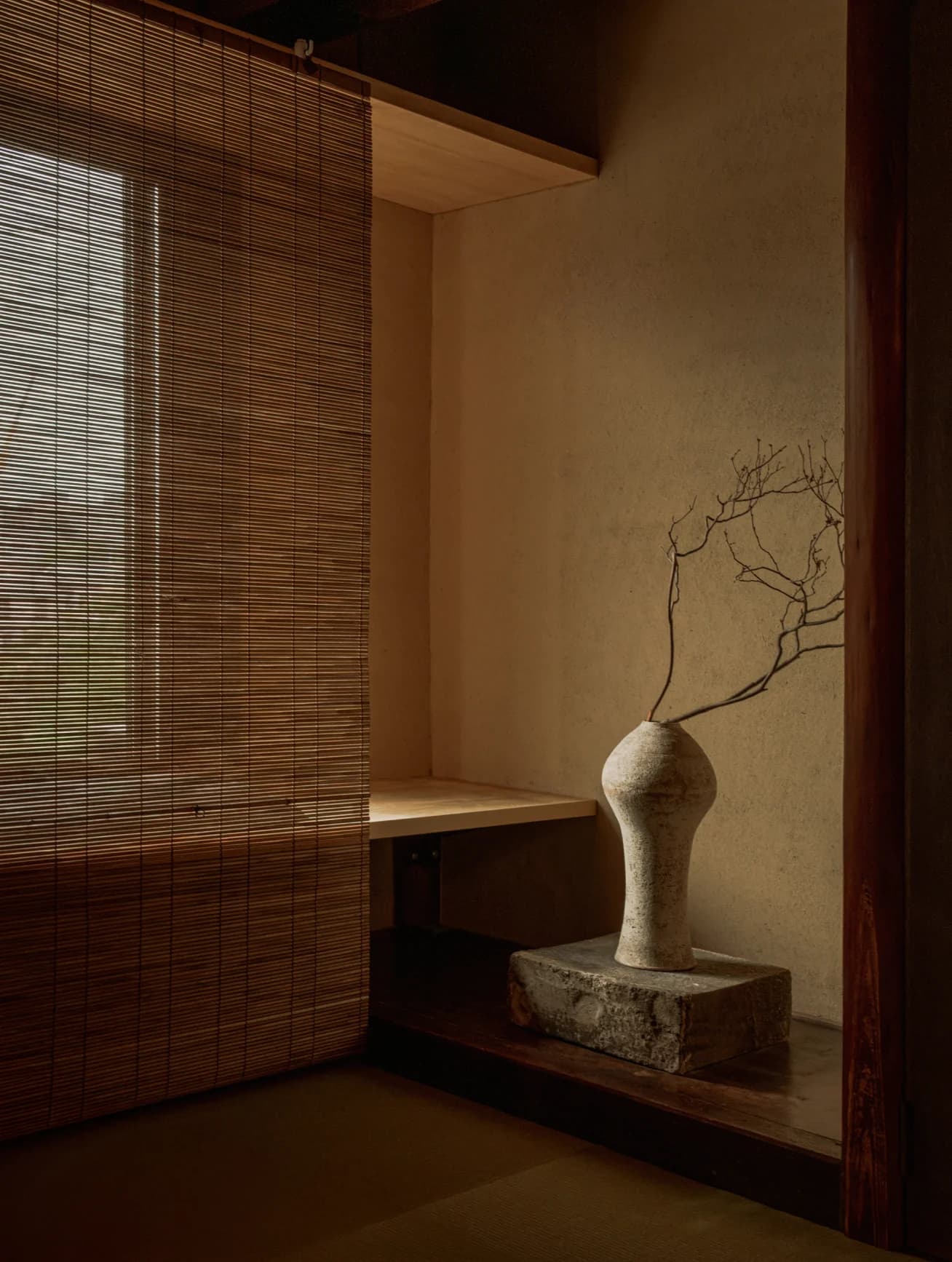Ceramic vase with branches in a tokonoma alcove beside a bamboo blind