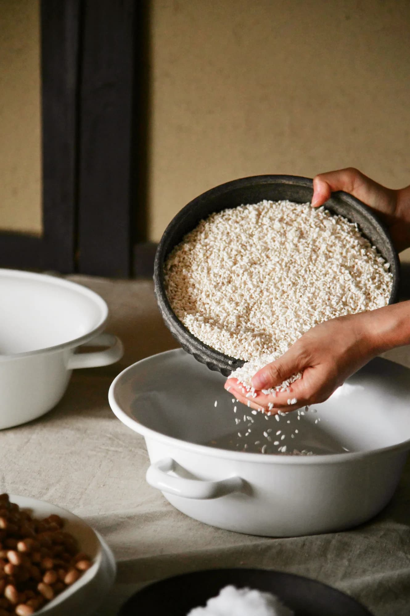 Hands pouring white rice from dark textured bowl into white ceramic bowl