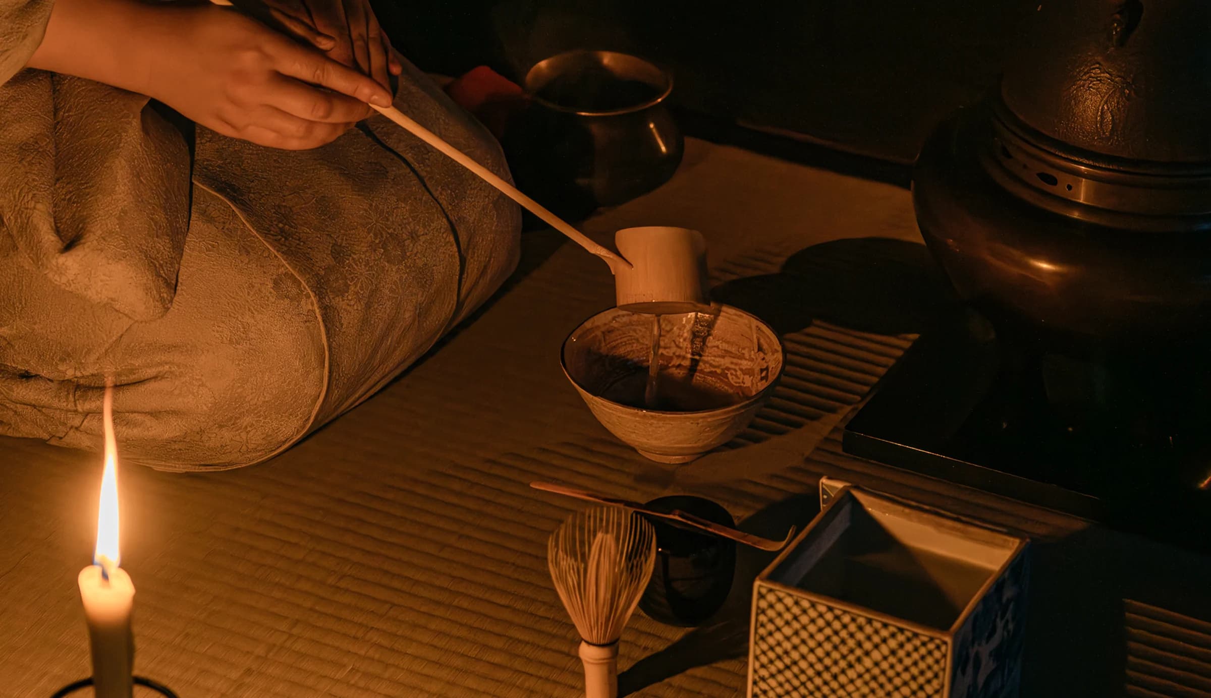 Woman in traditional Japanese clothing preparing tea by candlelight