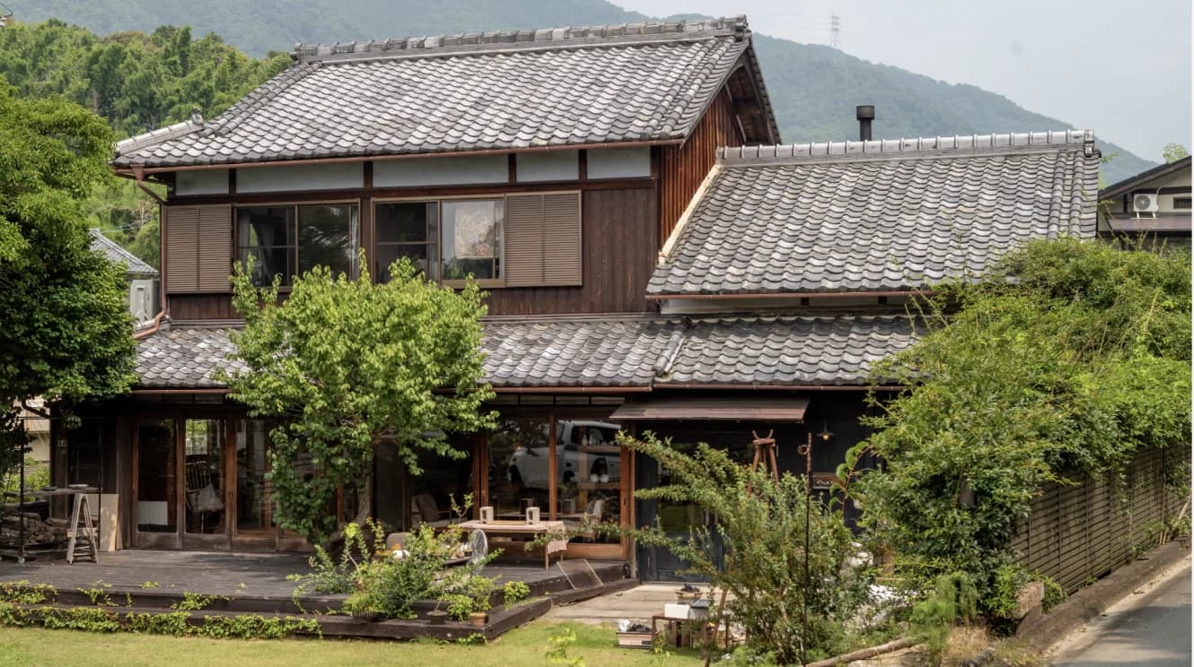 Traditional Japanese house with dark tiled roof nestled among lush green trees and mountains