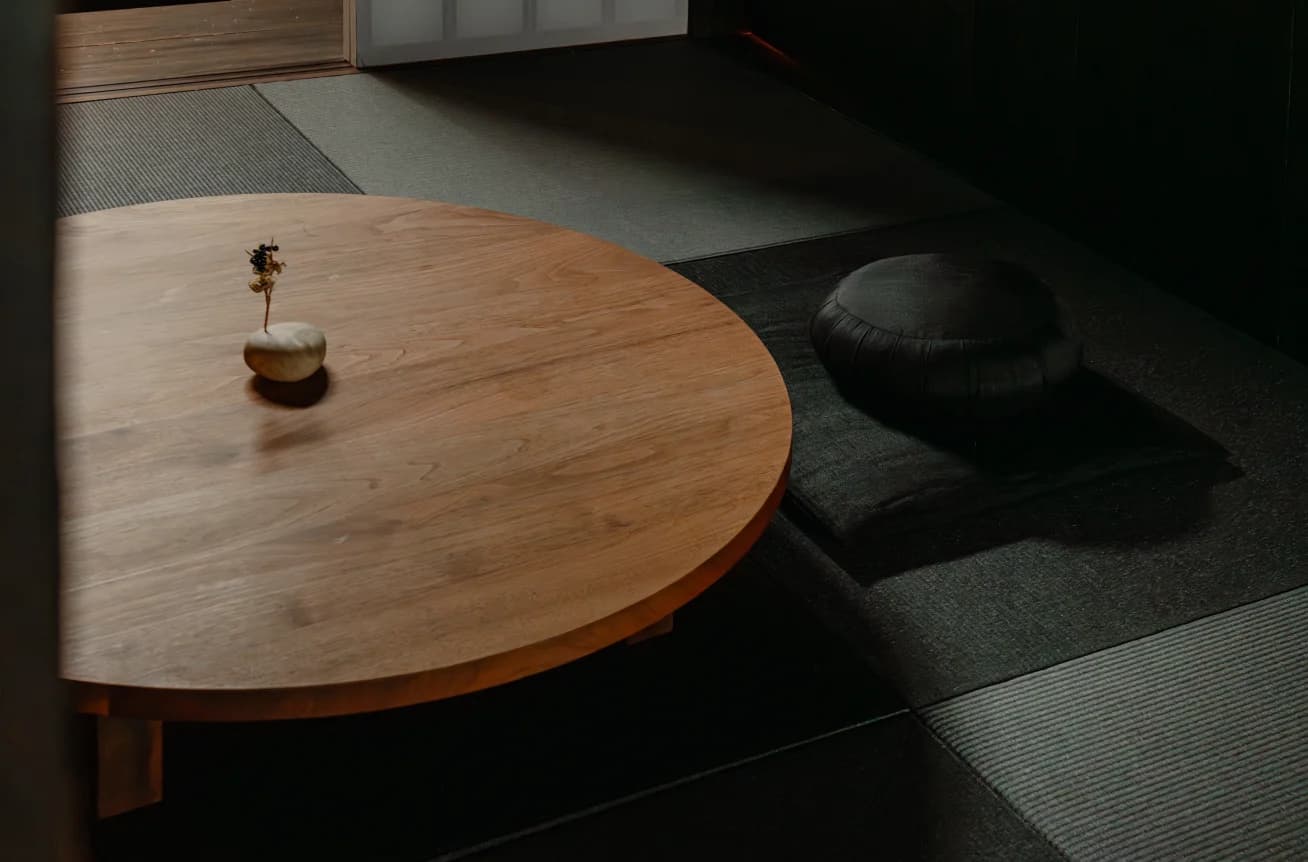 Round wooden low table with small vase on tatami floor with cushion