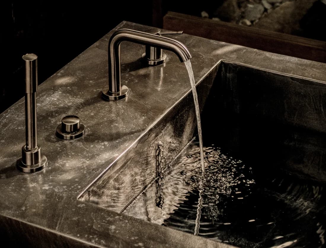 Stone basin faucet with water running, lit from above